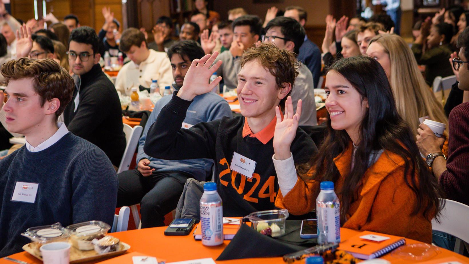 Recent alumni seated in Chancellor Green raise their hands to volunteer