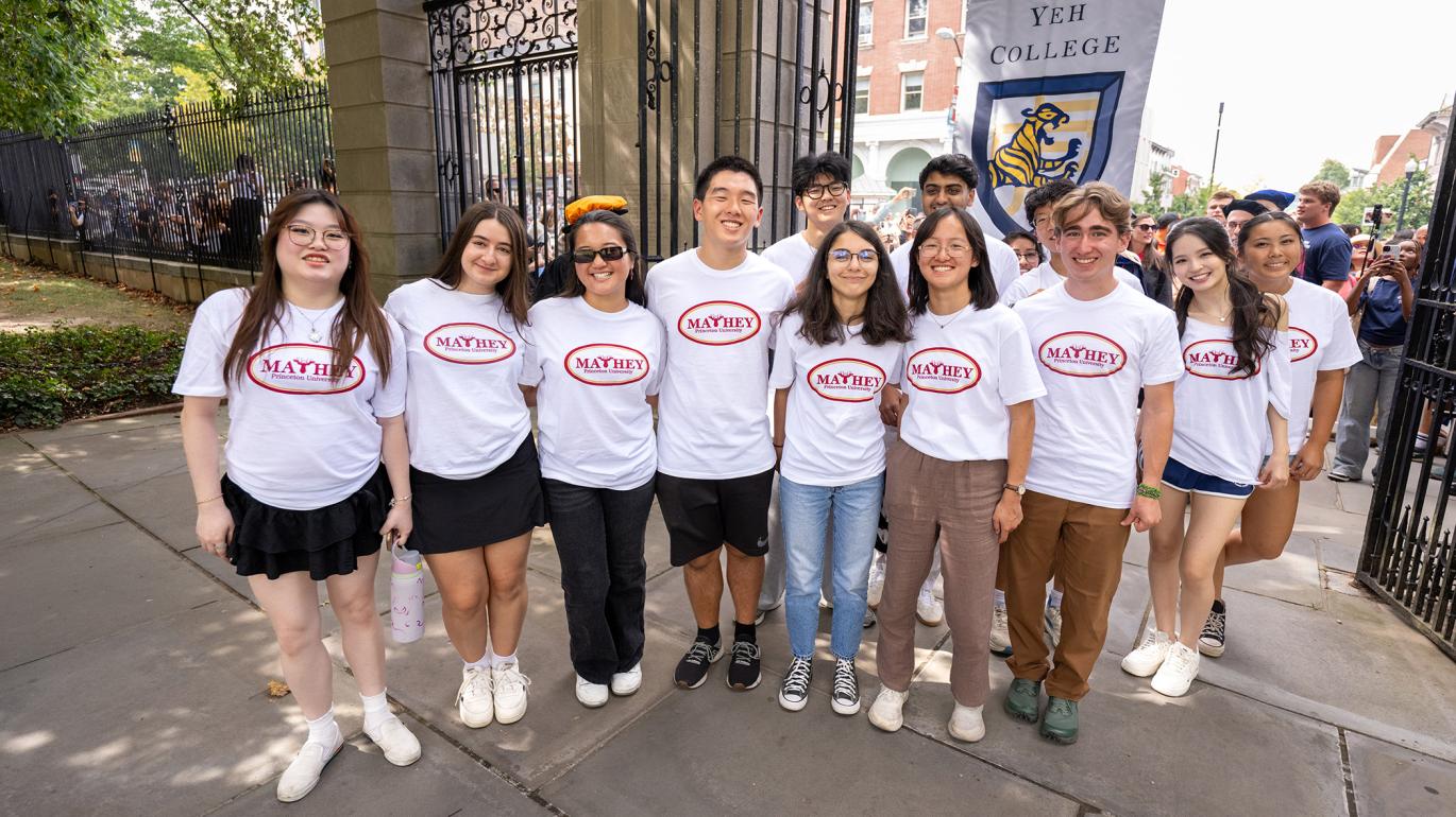 A group of new Princeton students wearing Mathey College white t-shirts pose together on the campus side of FitzRandolph Gate