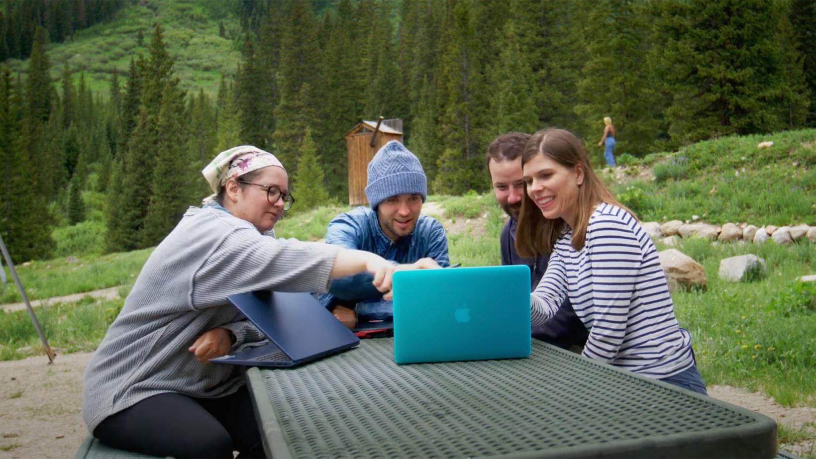 Cassie Stoddard with her students, in the woods, looking at their computer. 