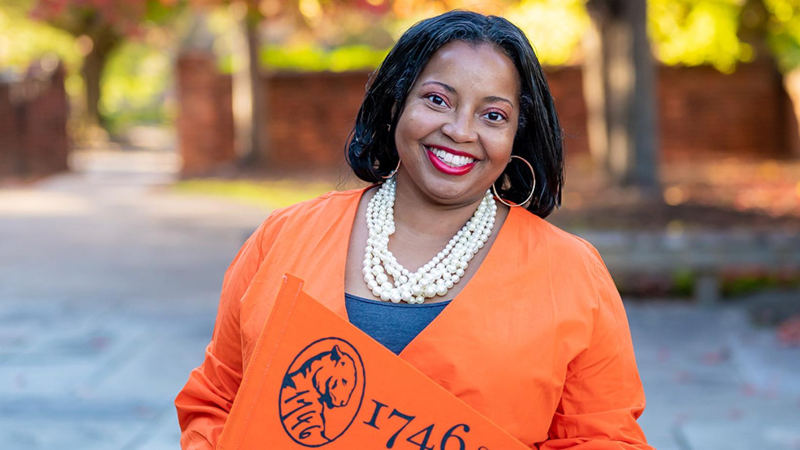 Jackie Bruce smiling and holding an orange 1746 Society pennant