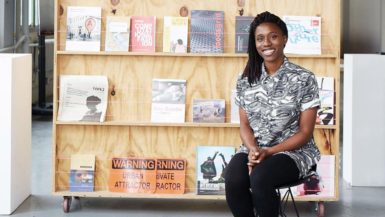 Mimi Onuoha smiling, sitting in front of some of her art projects.