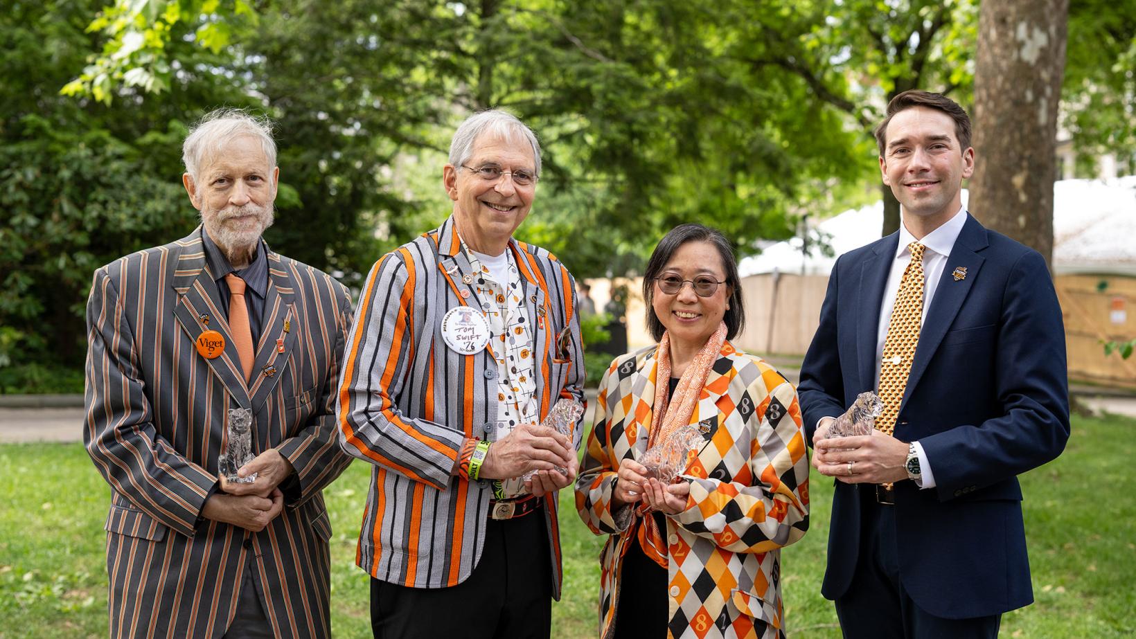 Three men and one woman stand outside holding crystal tigers