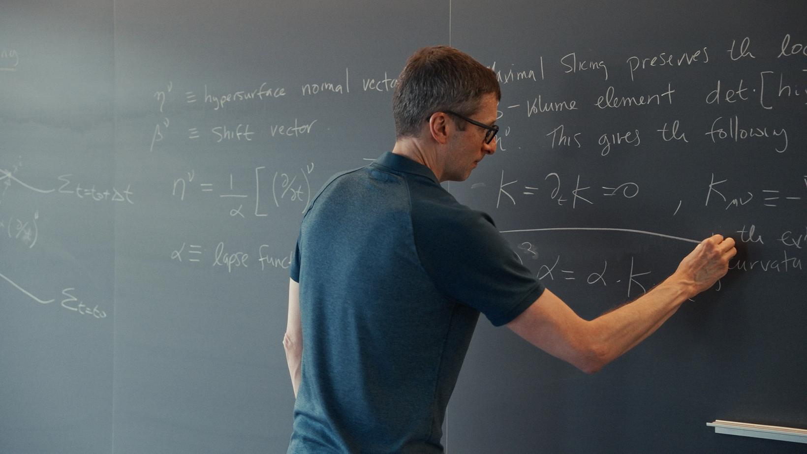 A male professor calculates advanced math equations on a classroom chalkboard.