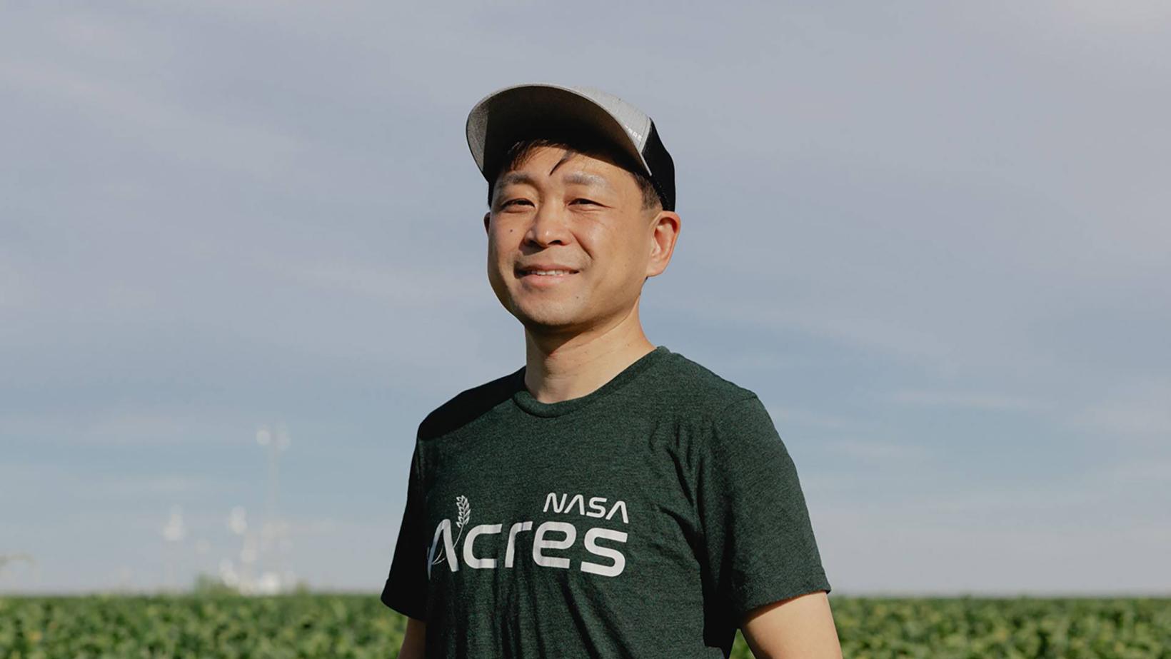 Asian male in baseball hat, standing in a farm field surrounded by green crops