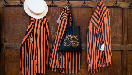 Orange and black Princeton jackets hanging on hooks on wood-paneled wall. 