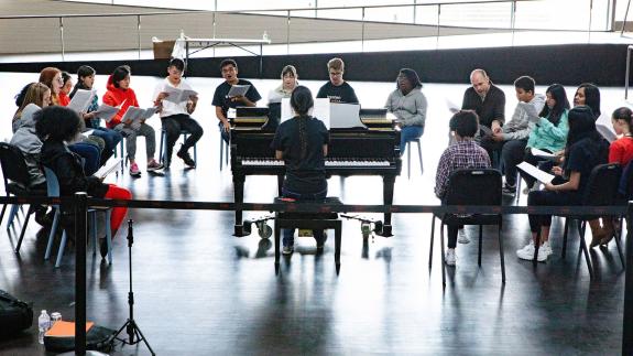 Trenton students sing together around a piano at the Lewis Arts complex.