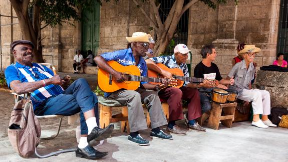 Image of 5 people in Havana sitting, two are playing the guitar 