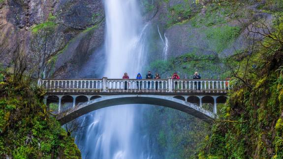 Multnomah Falls Bridge with a few people standing on the bridge and waterfall behind the bridge
