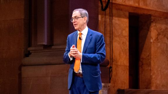 President Eisgruber, wearing a blue suit, speaking on the stage of Richardson Auditorium
