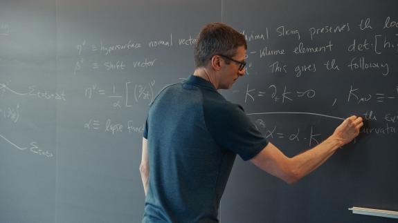 A male professor calculates advanced math equations on a classroom chalkboard.