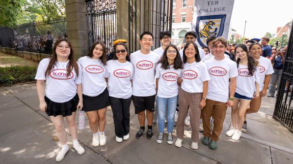 A group of new Princeton students wearing Mathey College white t-shirts pose together on the campus side of FitzRandolph Gate