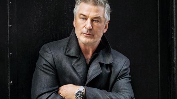 Alec Baldwin crosses his arms. He is wearing a black jacket.
