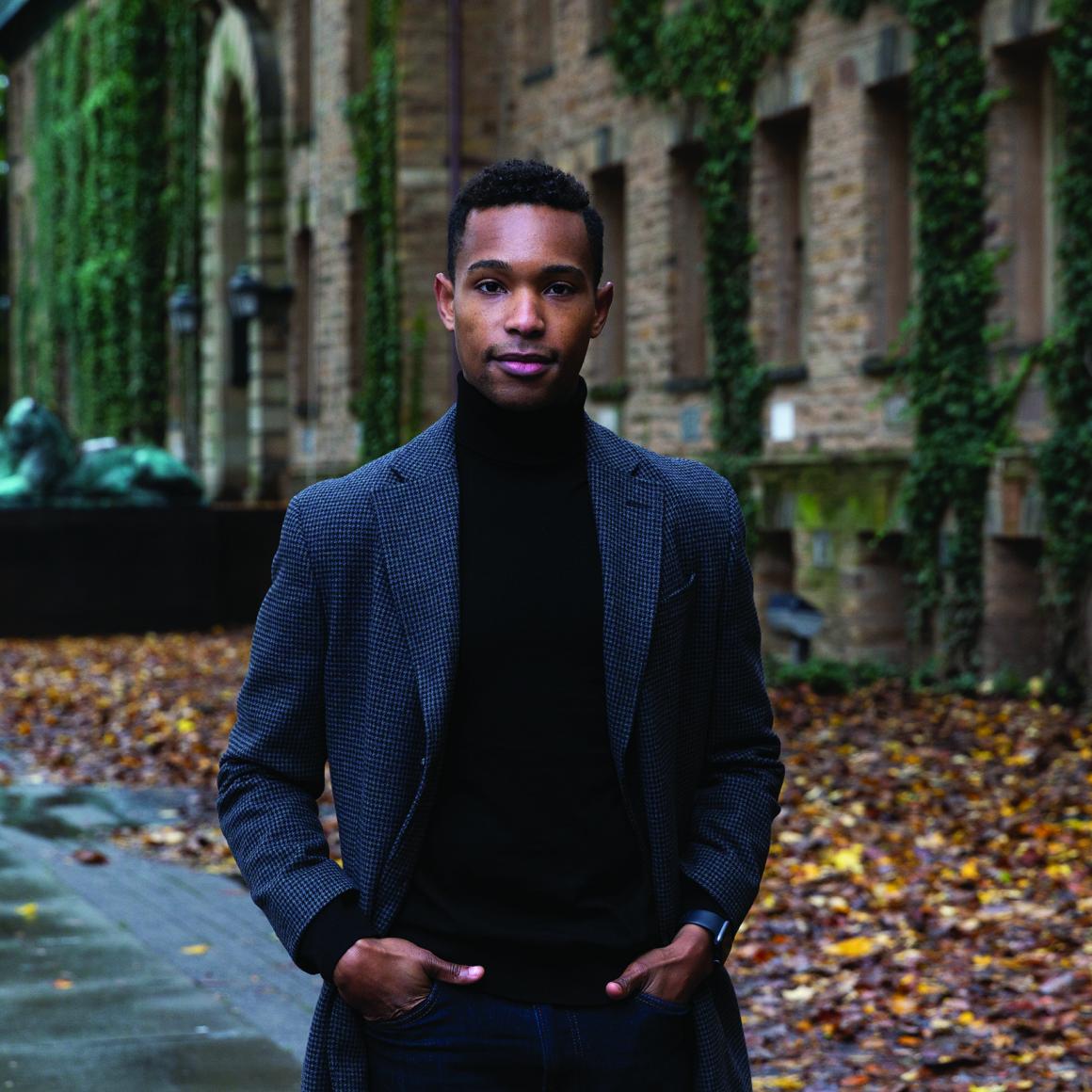 Christopher Hilare '24 stands in front of Nassau Hall; autumn leaves on ground