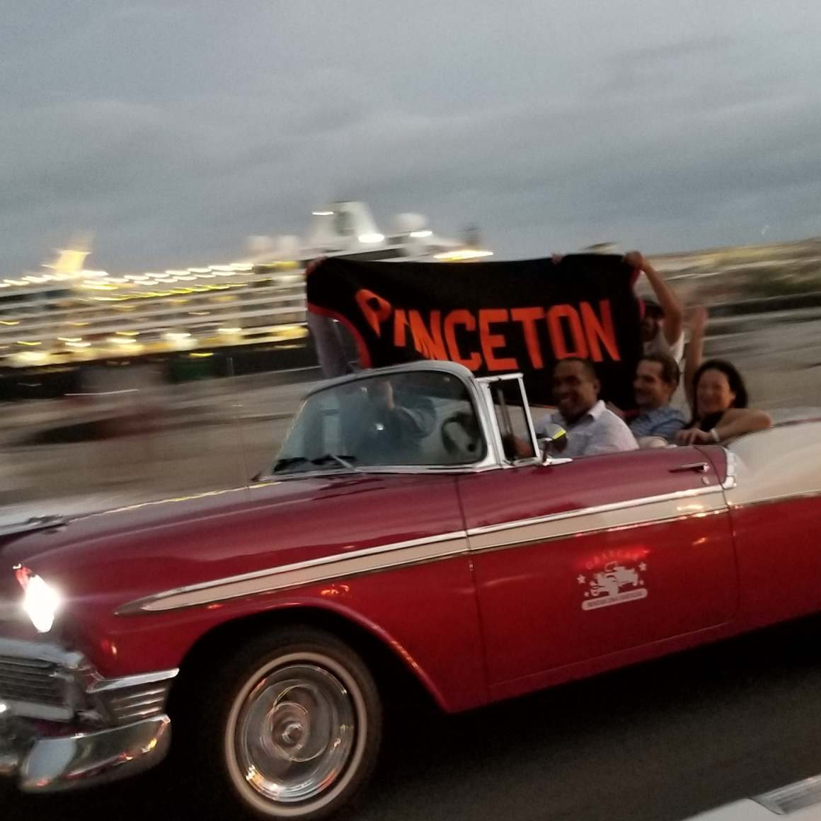 Travelers with Princeton banner driving red vintage car in Cuba