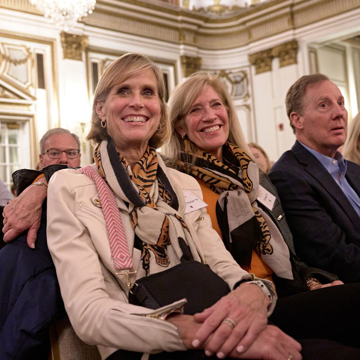 Two alumna smiling from their seats at the Boston event.