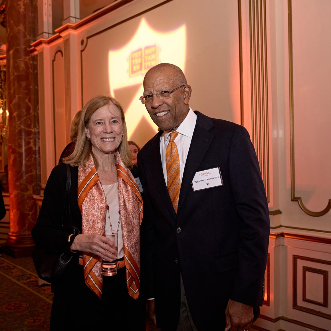 Two alumni posing in front of the orange Princeton logo.