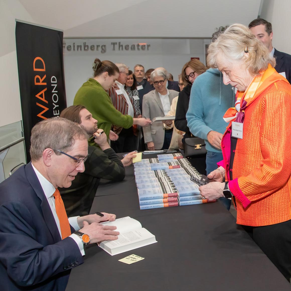 President Eisgruber signs copies of his book for a line of alumni.
