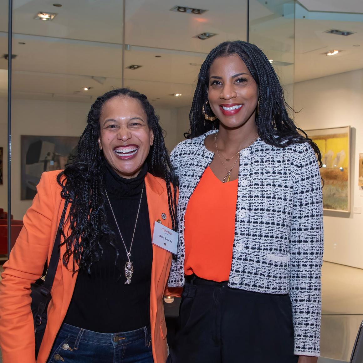 Two alumnae dressed in orange.