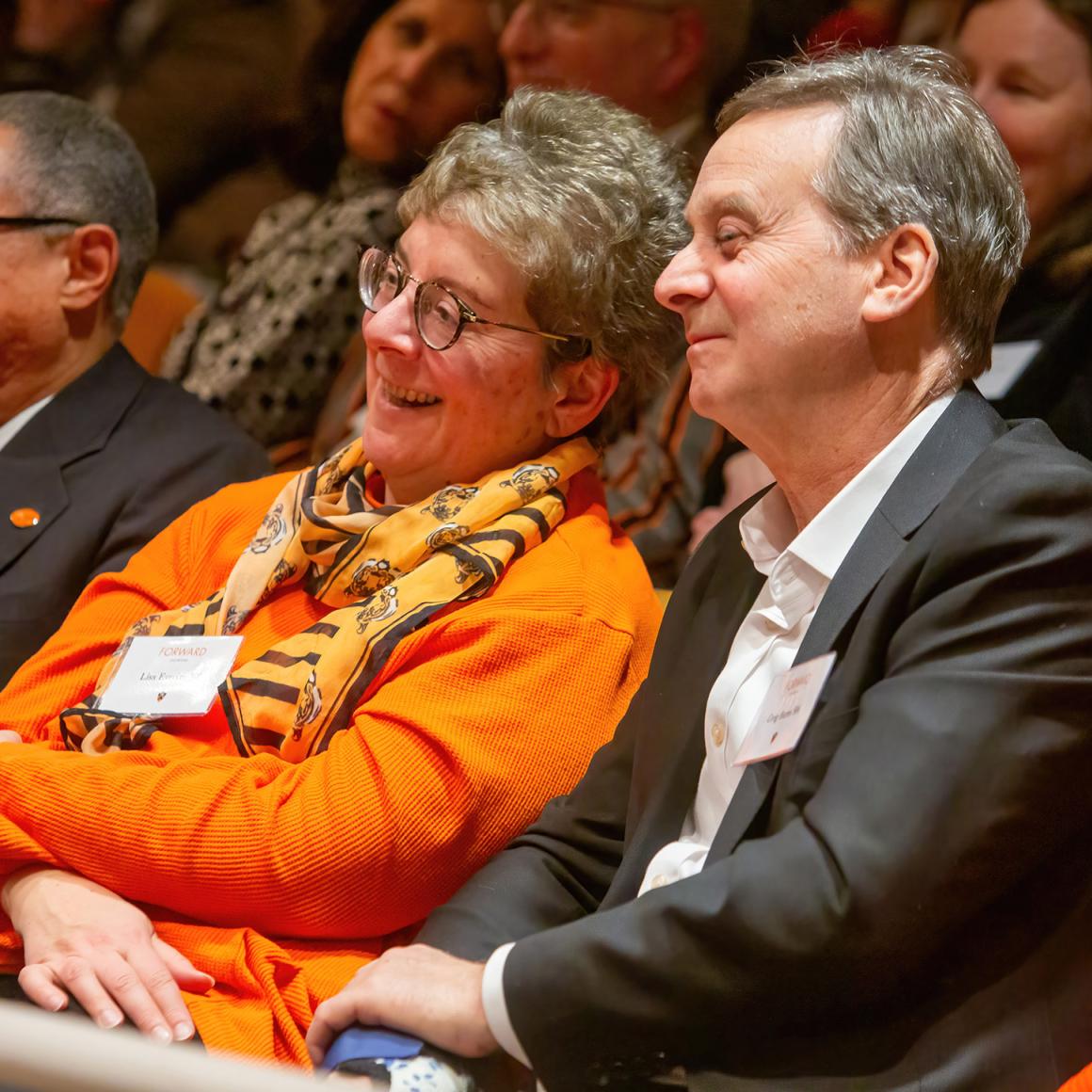 An alumna wearing bright orange smiles from the audience. 