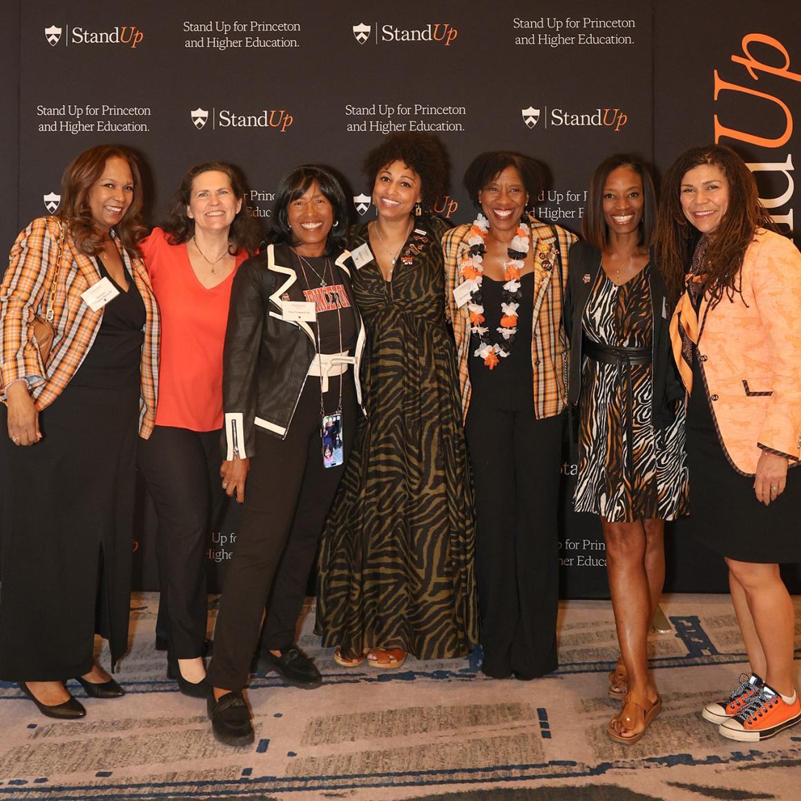 Seven alumni posing in front of the Stand Up for Princeton background