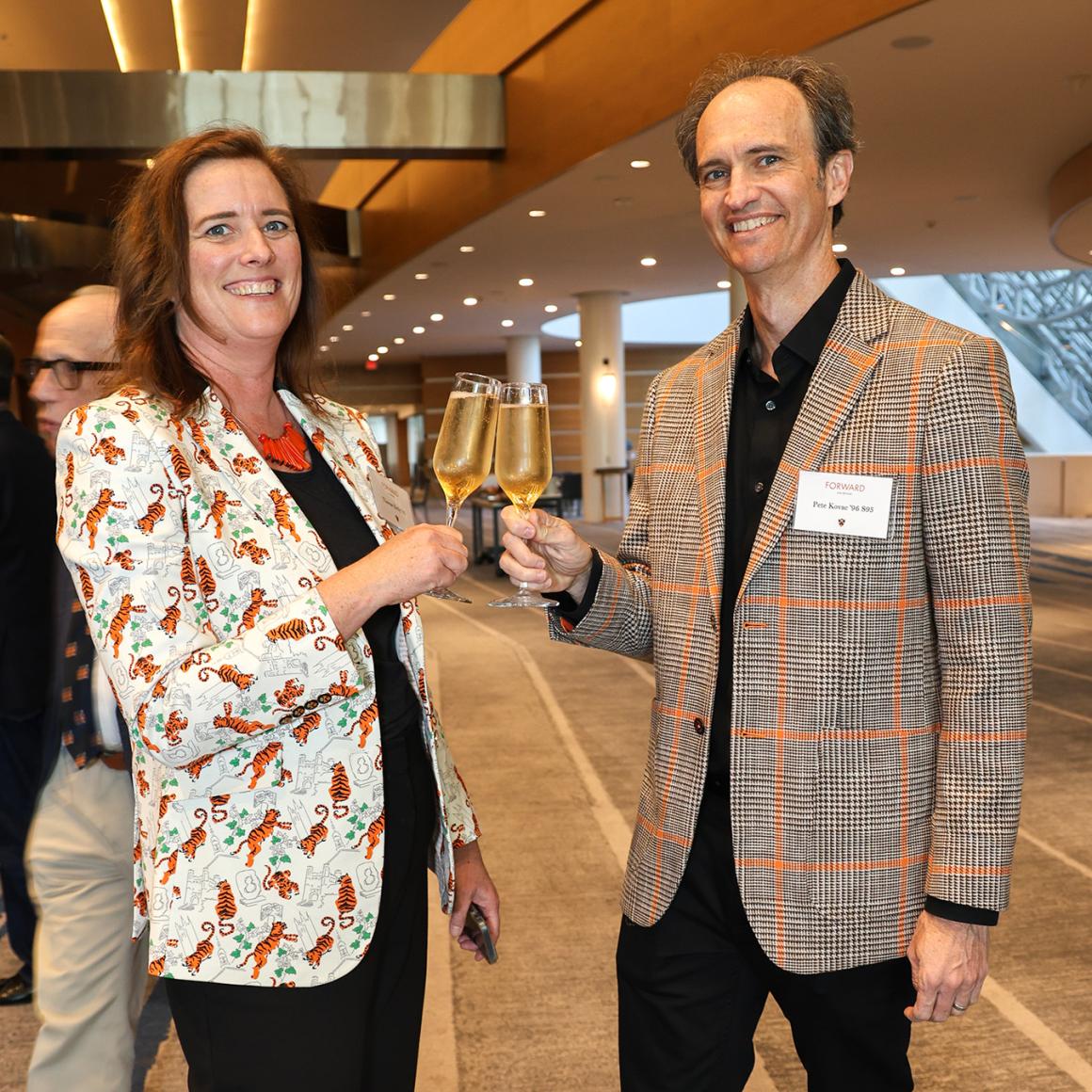 An alumni couple toasts wine glasses