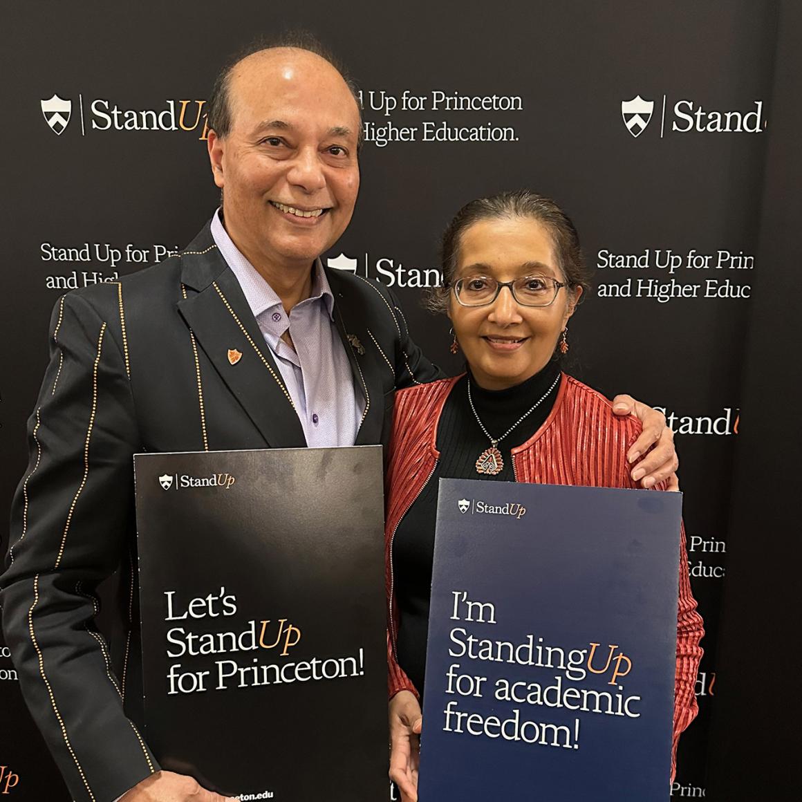 An alumni couple, dressed in orange and black, holding Stand Up for Princeton signs