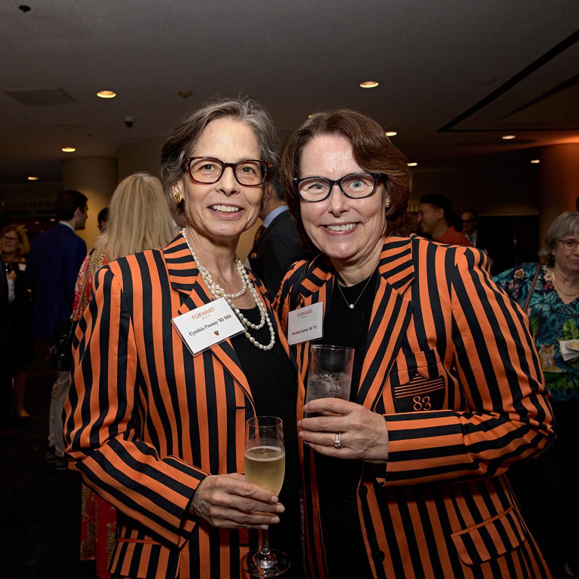 Two alumnae in matching orange and black striped class jackets