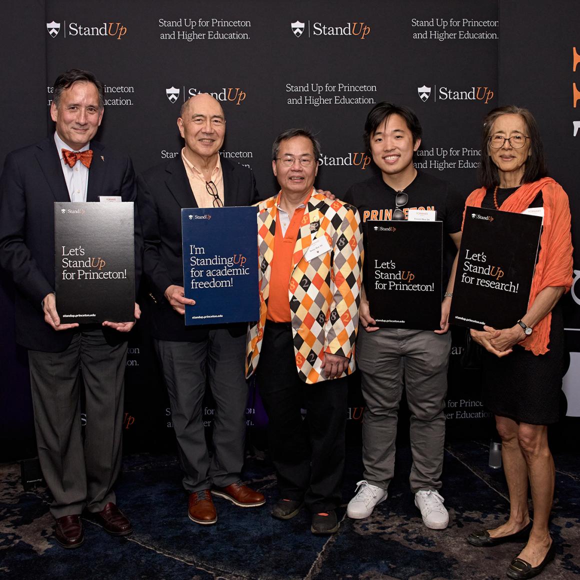 Five Princetonains in snazzy orange and black outfits hold signs supporting the Stand Up for Higher Education campaign