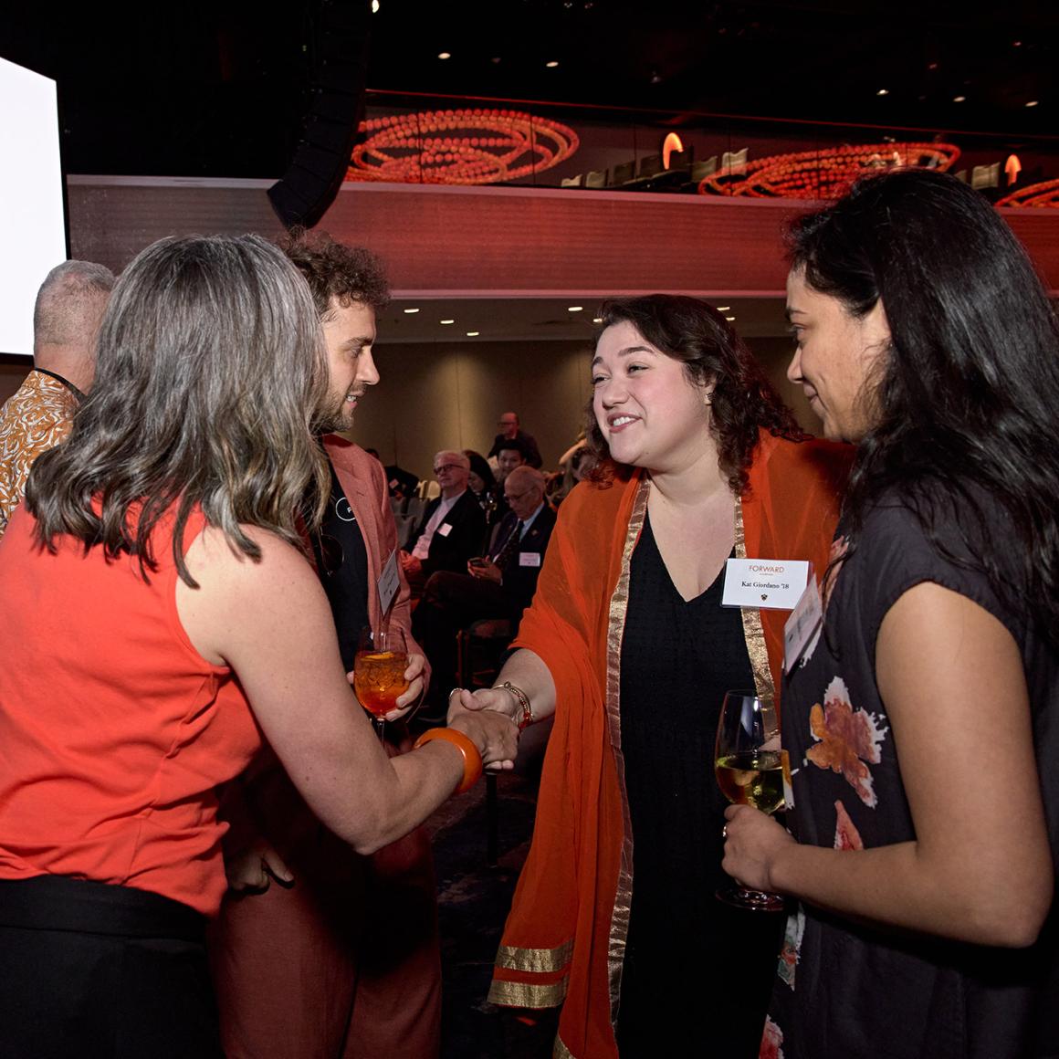 Kat Giordano shakes hands with another alumna in a crowded banquet hall. 