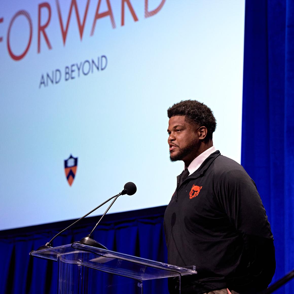 Standing in front of a giant Forward and Beyond projected image, Erik Plummer speaks to a Princeton alumni audience 