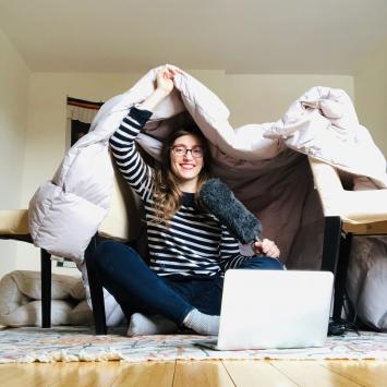 Stacey Vanek Smith sitting, holding a microphone and a blanket overhead