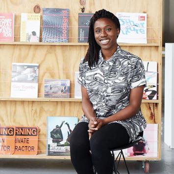 Mimi Onuoha smiling, sitting in front of some of her art projects. 
