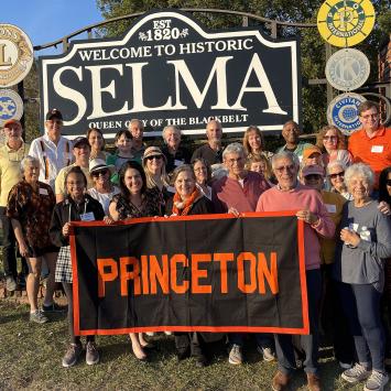 Princeton alumni and friends pose with a Princeton banner in front of a welcome sign to Selma, Alabama