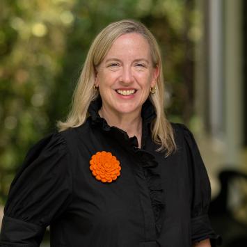 Jennifer Caputo, dressed in black and orange, standing on the porch of Maclean House