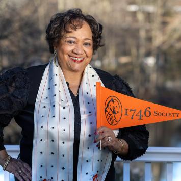 Juanita James, smiling, hand on hip, holding an orange 1746 Society pennant