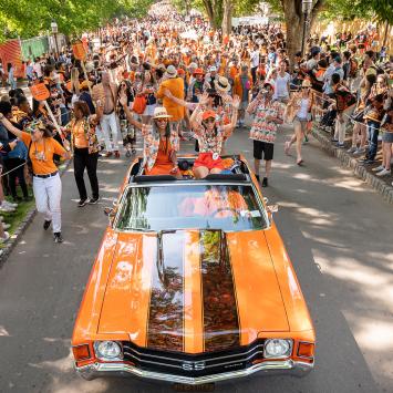 An orange convertible with black stripes is cheered by bystanders in the P-rade