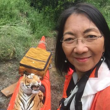 Elaine Chan headshot with a stuffed tiger in an orange kayak behind her