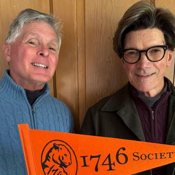 Guy Lawrence and his husband, holding an orange Princeton pennant