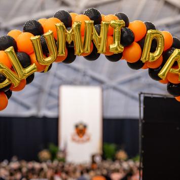 Orange and black balloon arch with balloon letters that say Alumni Day