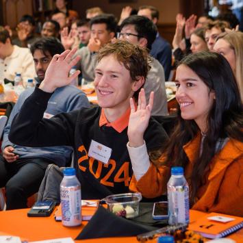 Recent alumni seated in Chancellor Green raise their hands to volunteer