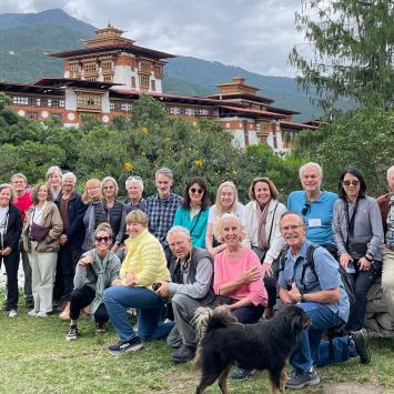 Kathy and Fred Miller with a group of fellow travelers outdoors in front of a building and mountain in Bhutan