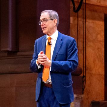 President Eisgruber, wearing a blue suit, speaking on the stage of Richardson Auditorium