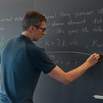 A male professor calculates advanced math equations on a classroom chalkboard.