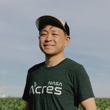 Asian male in baseball hat, standing in a farm field surrounded by green crops