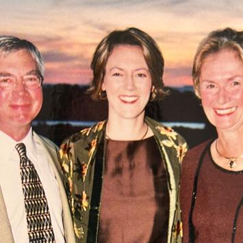 Three people stand together in front of a sky at sunset
