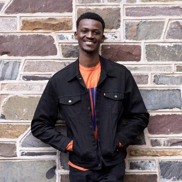 Godwin Obi, smiling and standing in front of stone exterior of academic building. 