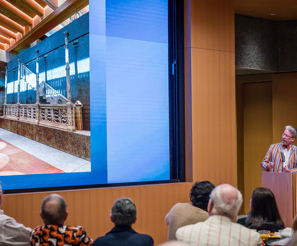 James Steward at a podium with a photo of the interior of the art museum on the screen to his left