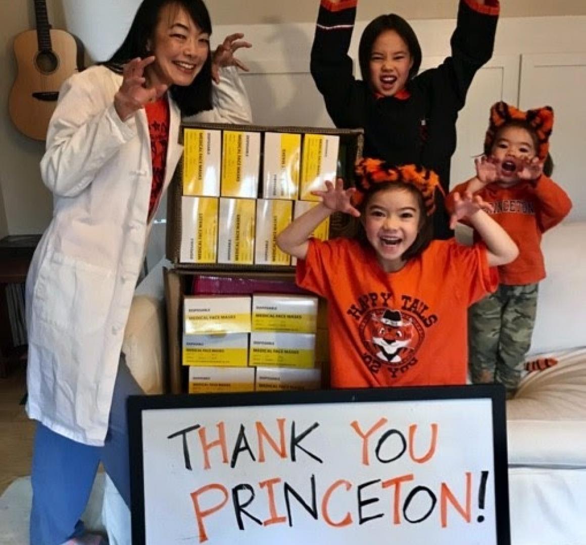 An adult and three youngsters imitate tiger grimaces and claws with PPE and thank you Princeton sign