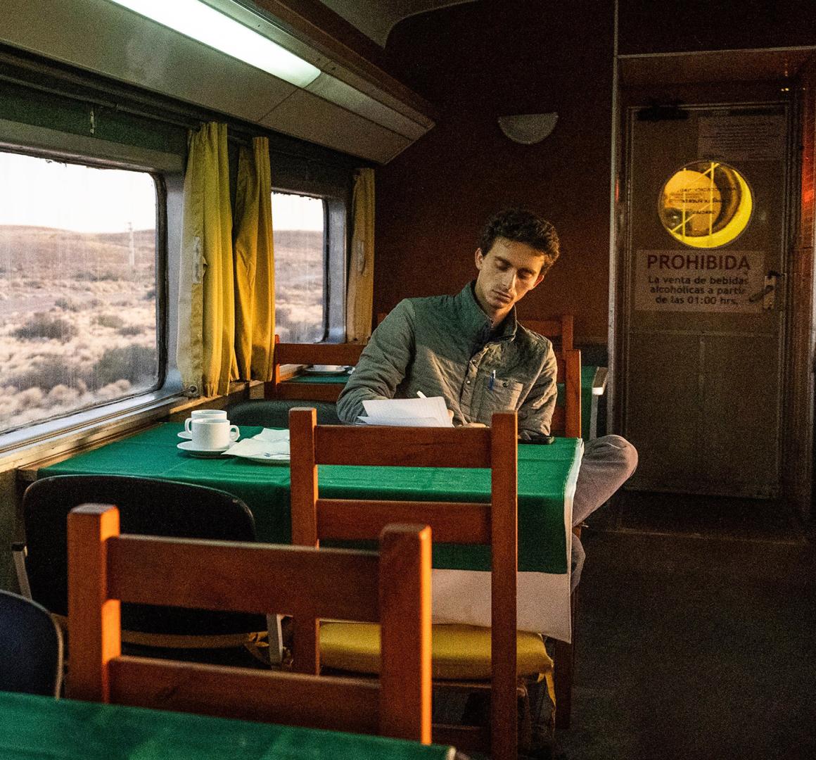 Jordan Salama writing at a table inside among train.