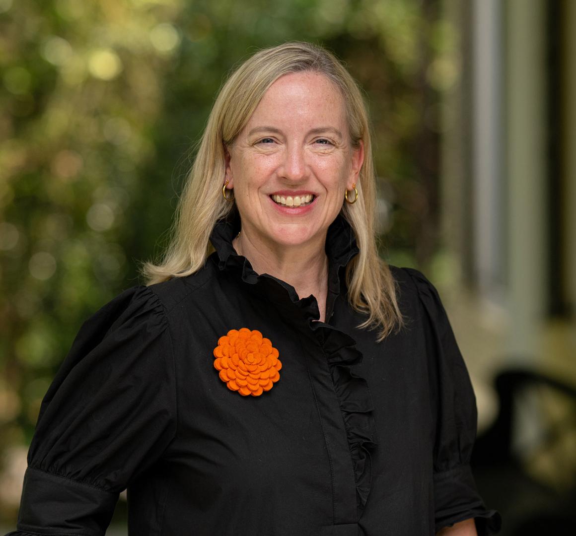 Jennifer Caputo, dressed in black and orange, standing on the porch of Maclean House